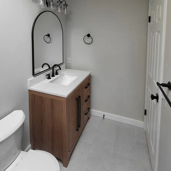 Bathroom with a wood vanity, arched black mirror, black fixtures and crown moulding under a skylight