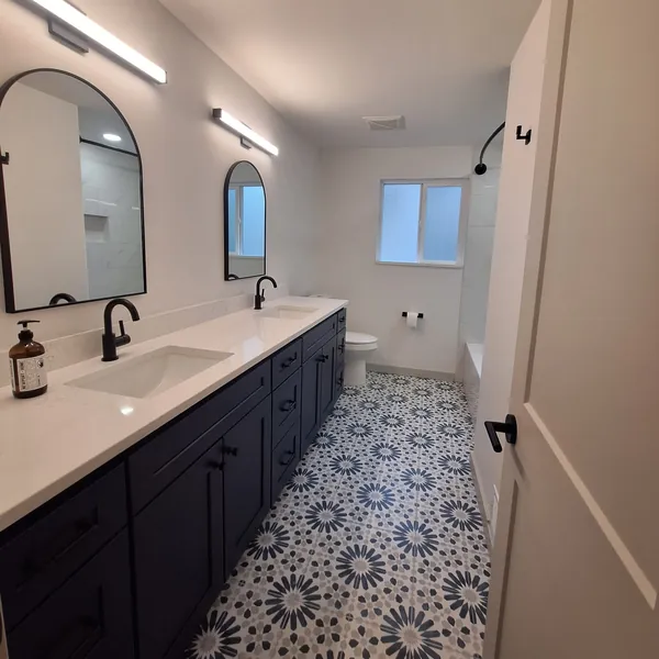 Bathroom with a navy double vanity, arched black-framed mirrors and a blue-and-white patterned tile floor