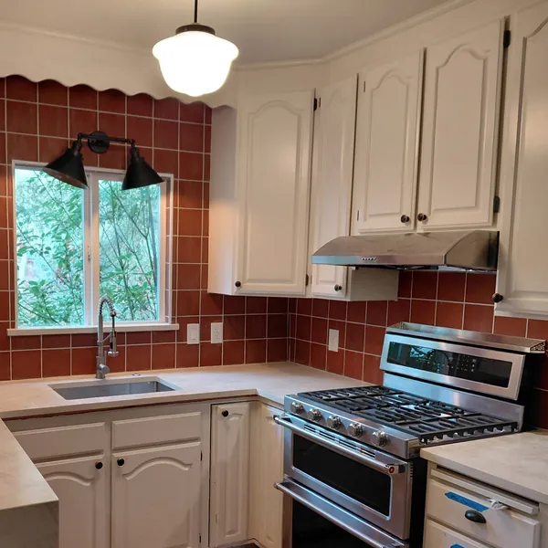 Kitchen with white cabinets, terracotta square tile backsplash, a schoolhouse pendant and a stainless gas range