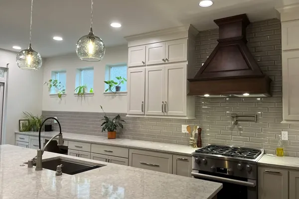 Finished kitchen with white shaker cabinets, a dark-stained wood range hood, gray beveled subway tile and a quartz island with glass pendant lights